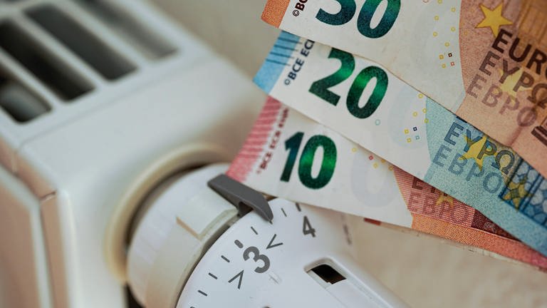 An ein Heizungs-Thermostat werden verschiedene Euro-Gelscheine gehalten. (Foto: IMAGO, IMAGO / Political-Moments)