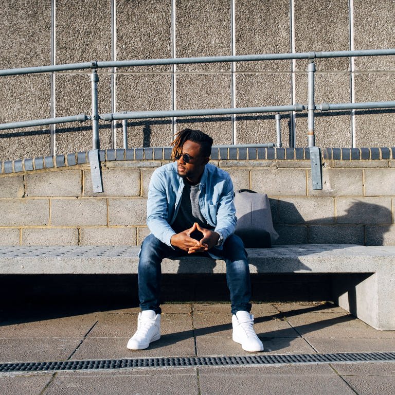 Young man sitting on concrete bench at sunny day model released, Symbolfoto (Foto: IMAGO, IMAGO / Westend61)