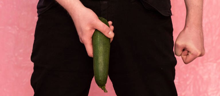 Ein Mann hält eine Zucchini als Penis an seine Hose (Foto: IMAGO, IMAGO / Elmar Gubisch)