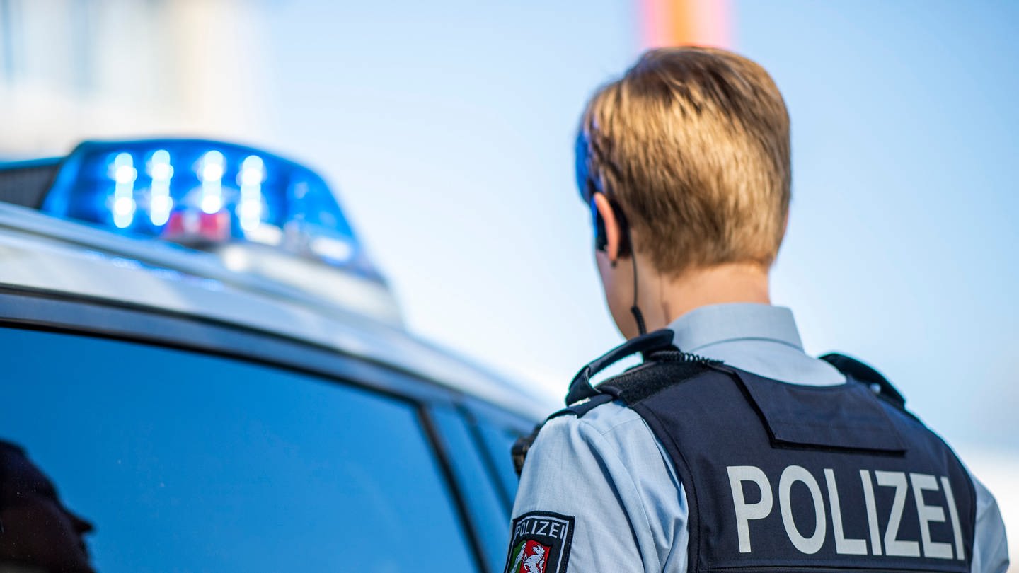 Eine Polizistin steht vor einem Streifenwagen, dessen Blaulicht leuchtet.