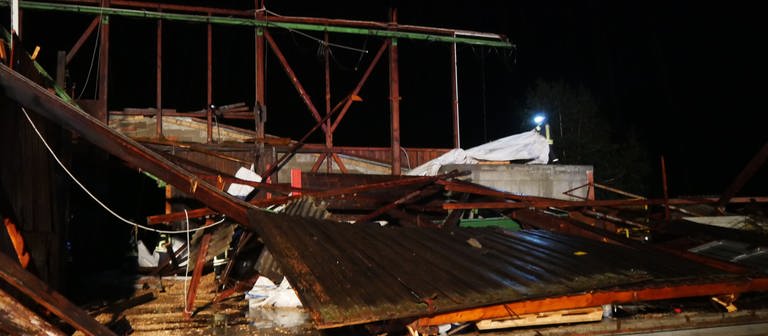Feuerwehrleute sichern die Überreste einer Lagerhalle. Bei einem Sturm wurde das Dach von einer Materialhalle weggefegt.  (Foto: DASDING, picture alliance/dpa/TNN | David Pichler)