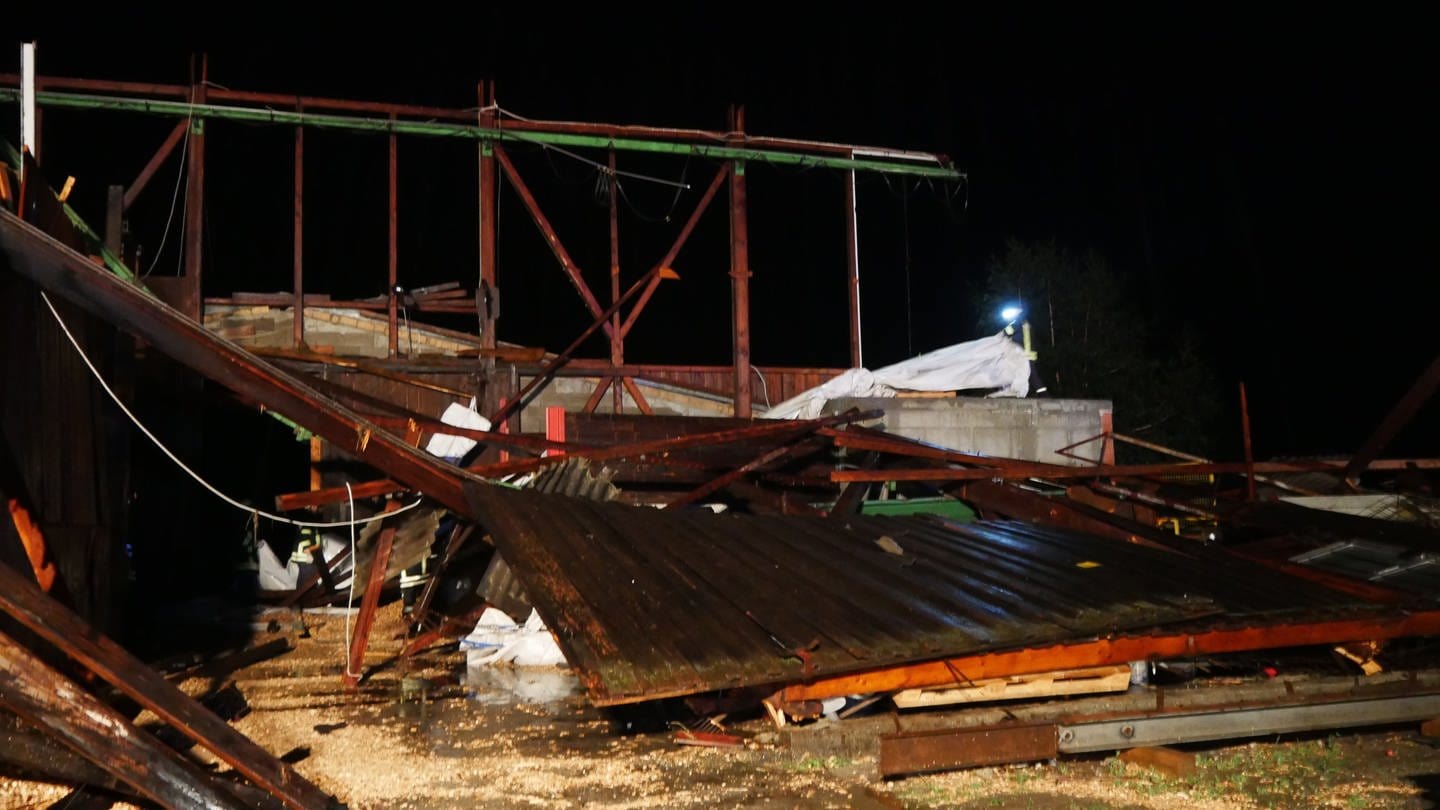 Feuerwehrleute sichern die Überreste einer Lagerhalle. Bei einem Sturm wurde das Dach von einer Materialhalle weggefegt. (Foto: DASDING, picture alliance/dpa/TNN | David Pichler)