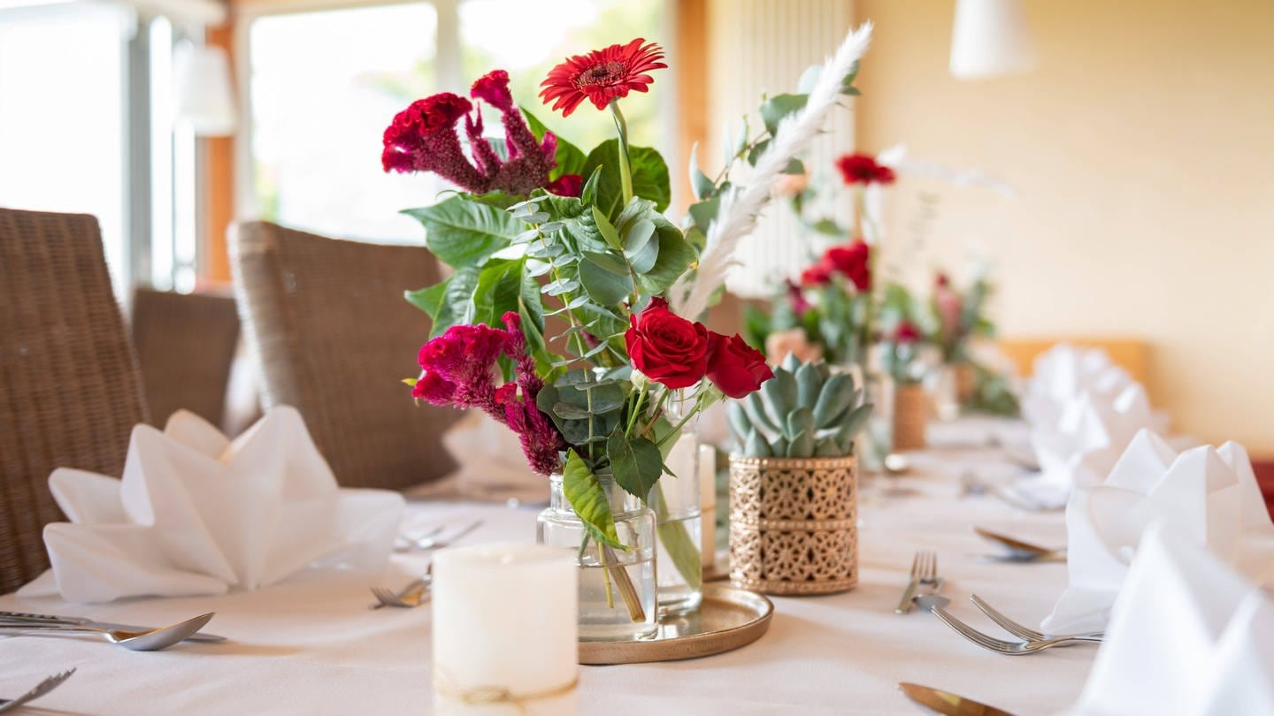 Rote Blumen stehen vor Beginn einer Hochzeitsfeier als Hochzeitsdekoration auf einem Tisch.