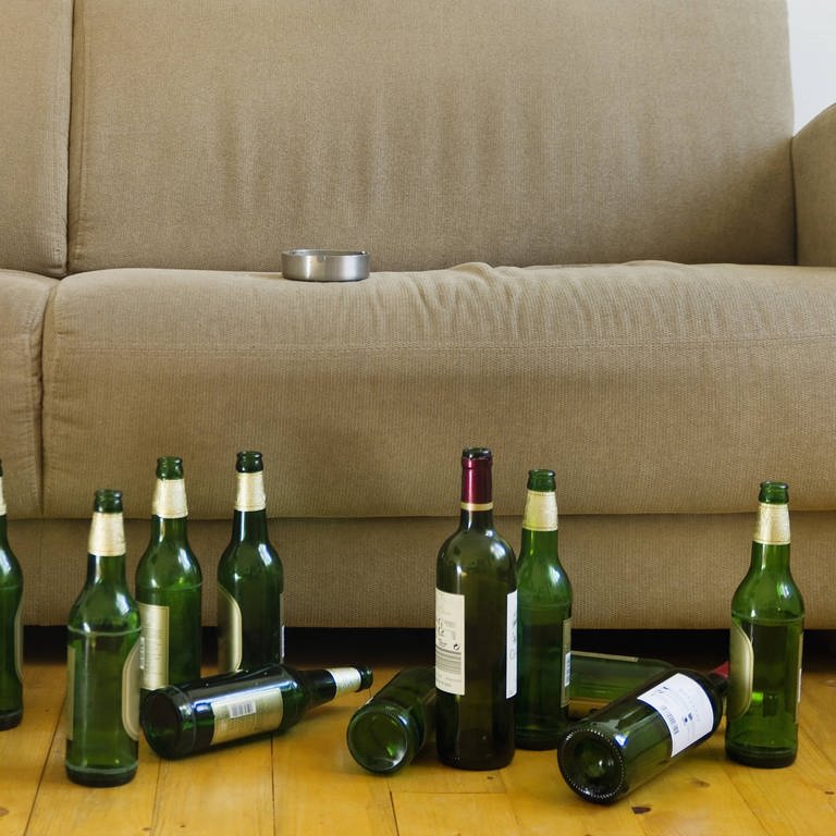 Vor einem Sofa stehen viele Bierflaschen und eine Weinflasche auf dem Boden. (Foto: IMAGO, IMAGO / Westend61)