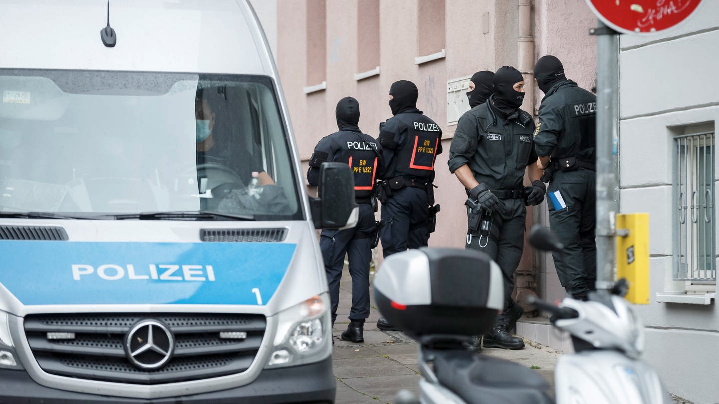 Polizisten stehen vor einem Hauseingang in Stuttgart. In sieben Städten in Baden-Württemberg haben in Zusammenhang mit Angriffen auf Teilnehmer einer Corona-Demonstration Razzien stattgefunden.
