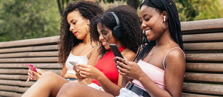 Junge Frauen mit Smartphones auf einer Bank: Was macht die Nutzung sozialer Netzwerke mit uns? (Foto: IMAGO, IMAGO / Addictive Stock)