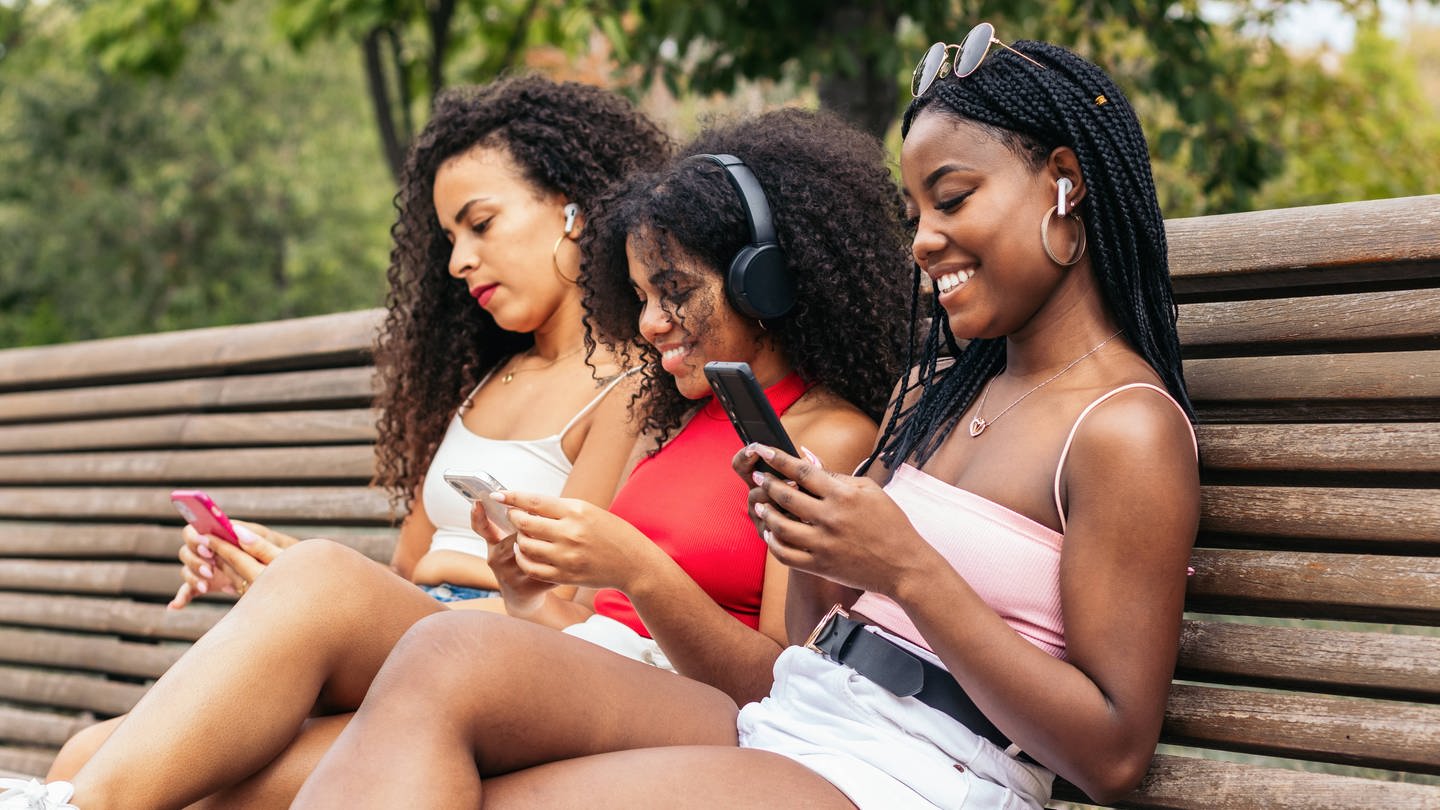 Junge Frauen mit Smartphones auf einer Bank: Was macht die Nutzung sozialer Netzwerke mit uns?