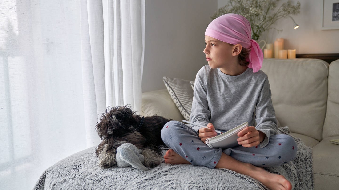 little child with cancer disease writing notes while sitting with dog on bed in room