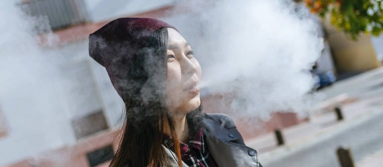 Young woman blowing out smoke from electronic cigarette model released Symbolfoto (Foto: IMAGO, IMAGO / Westend61)