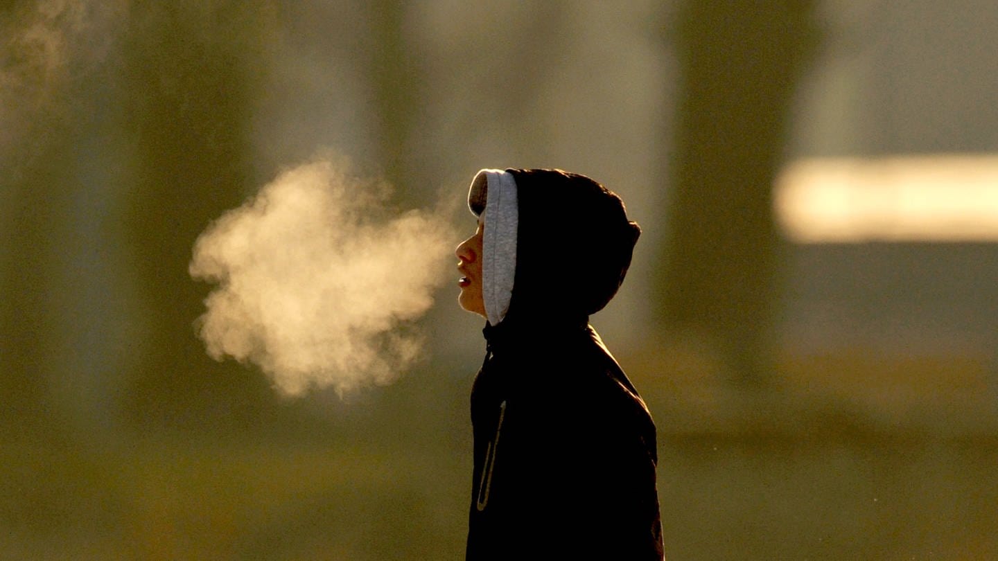 Ein Junge steht am Freitag auf dem zugefrorenen Maschsee in Hannover im Gegenlicht der aufgehenden Sonne, in dem sich sein Atem abzeichnet. (Foto: dpa Bildfunk, picture alliance / dpa | Julian Stratenschulte)