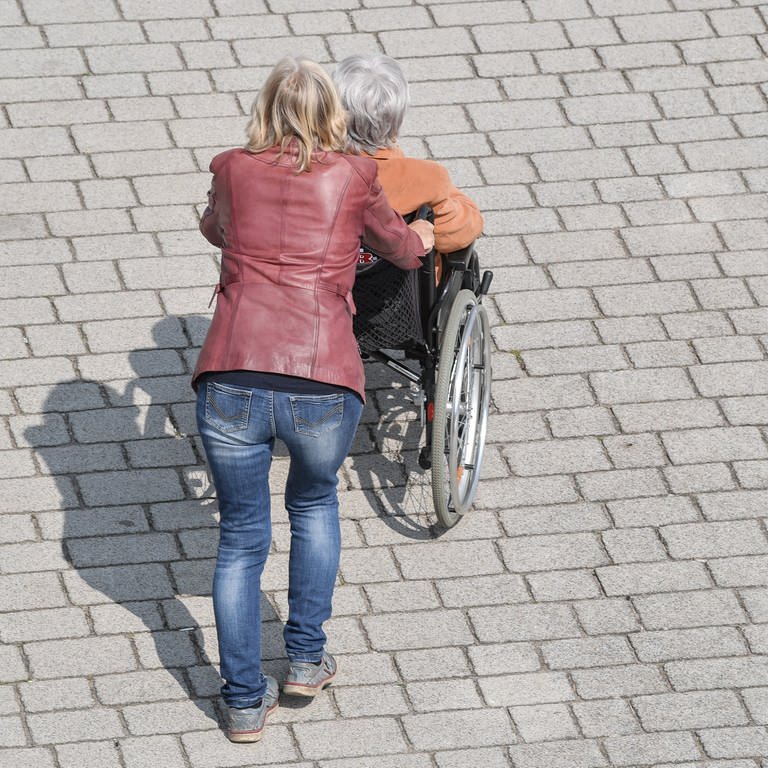 Eine Frau schiebt eine ältere Frau in einem Rollstuhl über einen Gehweg. (Foto: dpa Bildfunk, picture alliance/dpa/dpa-Zentralbild | Patrick Pleul)
