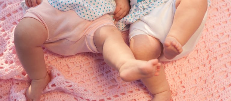 Zwei Zwillinge (Babys) liegen auf einer Decke. (Foto: IMAGO, agefotostock)
