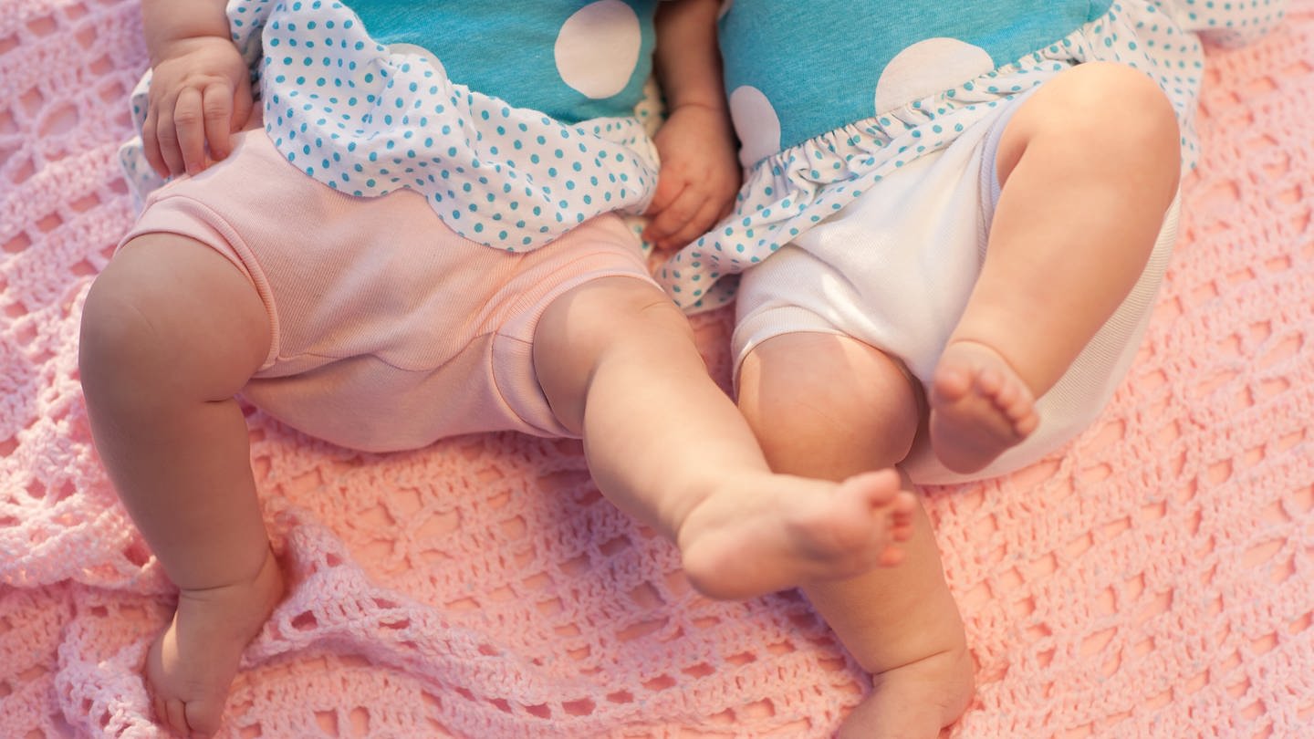 Zwei Zwillinge (Babys) liegen auf einer Decke.