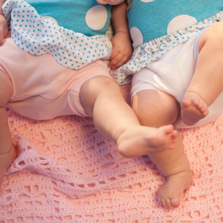 Zwei Zwillinge (Babys) liegen auf einer Decke. (Foto: IMAGO, agefotostock)