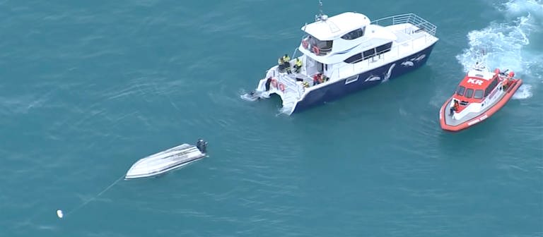 Eine Luftaufnahme eines Videos zeigt zwei Rettungsboote neben einem gekenterten Boot (Foto: dpa Bildfunk, picture alliance/dpa/TVNZ via AP | Uncredited)