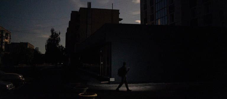 In der ukrainischen Stadt Pokrowsk läuft eine Person bei Nacht mit einer Taschenlampe an einem Gebäude vorbei. (Foto: dpa Bildfunk, picture alliance/dpa/AP | Leo Correa)
