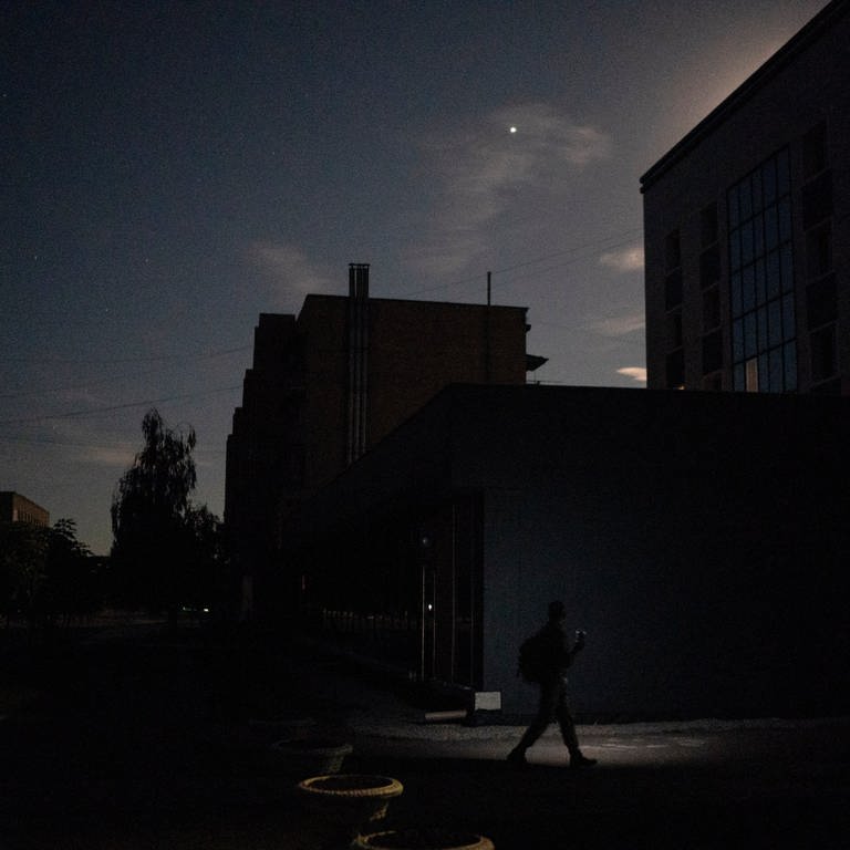 In der ukrainischen Stadt Pokrowsk läuft eine Person bei Nacht mit einer Taschenlampe an einem Gebäude vorbei. (Foto: dpa Bildfunk, picture alliance/dpa/AP | Leo Correa)