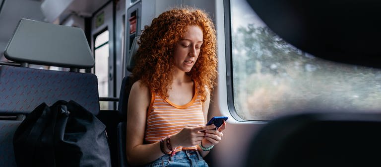 Ein Frau sitzt im Zug. (Foto: IMAGO, IMAGO / Addictive Stock)