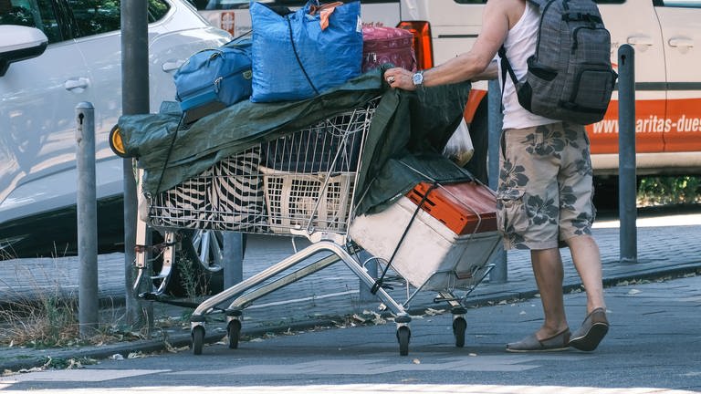 Ein wohnungsloser Mensch läuft mit Einkaufswagen voll Tüten auf der Straße (Foto: IMAGO, Michael Gstettenbauer)
