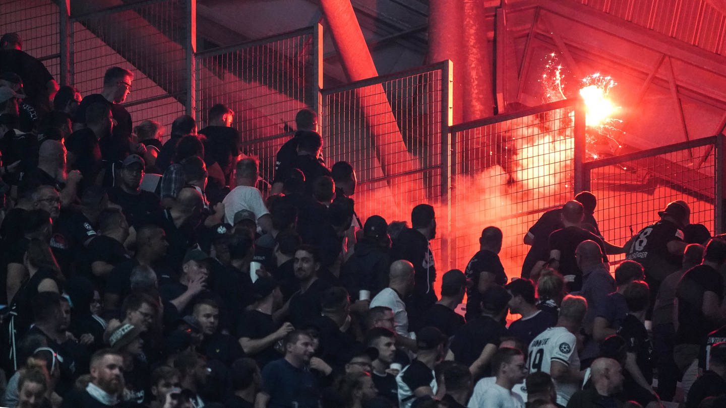 Fußballfans stehen beim Champions-League-Spiel zwischen Marseille und Frankfurt in einem Zuscherblock im Stade Velodrome in Marseille, hinter einem Zaun brennt Pyrotechnik.