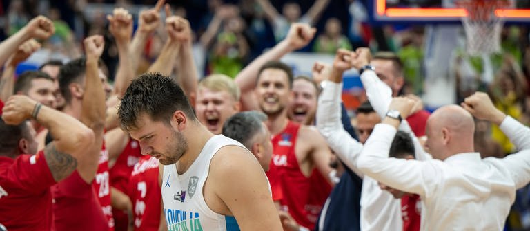 Basketballer Luka Doncic nach dem Spiel gegen Polen bei der EM mit hängendem Kopf. Im Hintergrund feiert die polnische Mannschaft (Foto: IMAGO, IMAGO / camera4+)