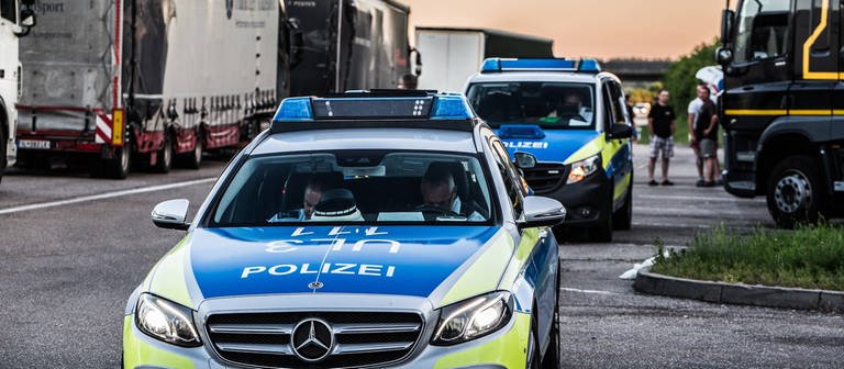 Auf einem Rasthof an einer Autobahn stehen zwei Polizeiautos zwischen geparkten Lkw. (Foto: IMAGO, IMAGO / onw-images)