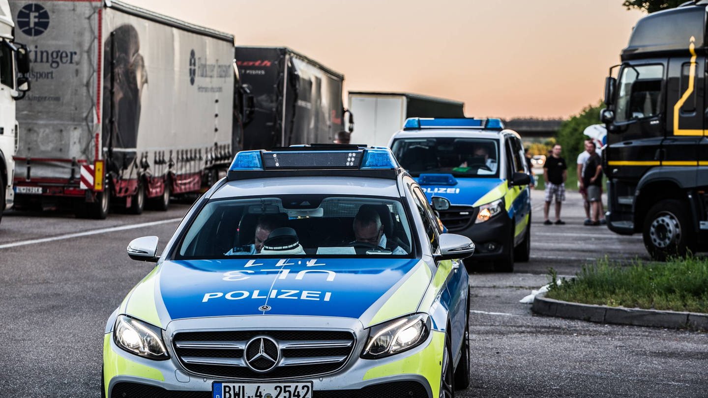 Auf einem Rasthof an einer Autobahn stehen zwei Polizeiautos zwischen geparkten Lkw.