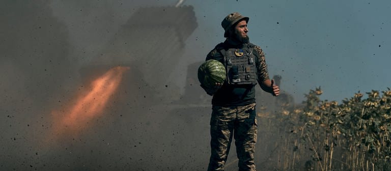 Ukrainischer Soldat mit Melone in der Hand; im Hintergrund Raketenwerfer (Foto: picture-alliance / Reportdienste, picture alliance/dpa/AP | Kostiantyn Liberov)
