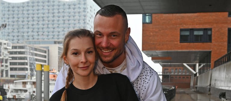 Eric Sindermann und seine Freundin Katharina lächeln im Hamburger Hafen für ein Foto. (Foto: IMAGO, IMAGO / Andre Lenthe)