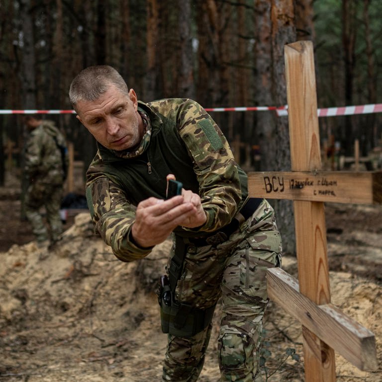 Oleg Kotenko, der Beauftragte für Vermisstenfragen unter besonderen Umständen, filmt mit seinem Smartphone das Grab eines ukrainischen Soldaten in Isjum. (Foto: dpa Bildfunk, Evgeniy Maloletka)