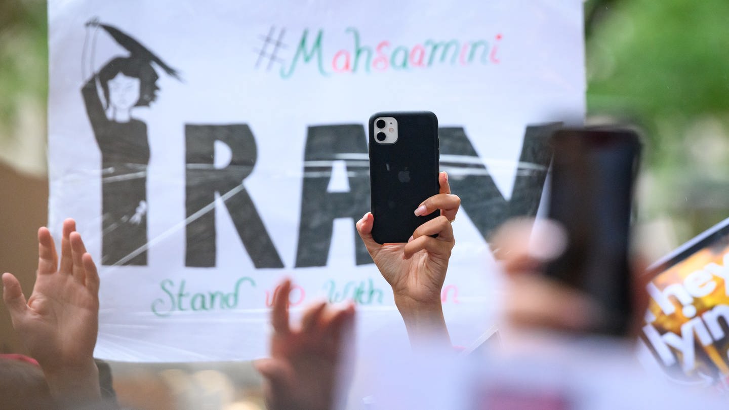 Ein Smartphone wird vor einem Plakat in die Höhe gehalten auf einer Solidaritätskundgebung nach dem Tod von Iranerin Mahsa Amini, die in der vergangenen Woche im Iran in Polizeigewahrsam gestorben war.