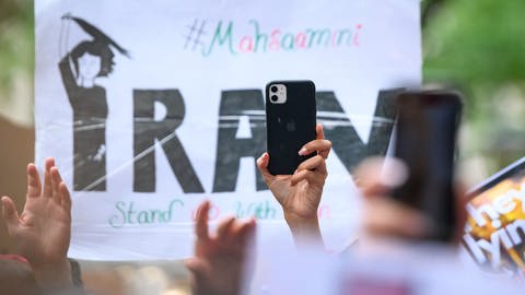 Ein Smartphone wird vor einem Plakat in die Höhe gehalten auf einer Solidaritätskundgebung nach dem Tod von Iranerin Mahsa Amini, die in der vergangenen Woche im Iran in Polizeigewahrsam gestorben war. (Foto: dpa Bildfunk, Picture Alliance)