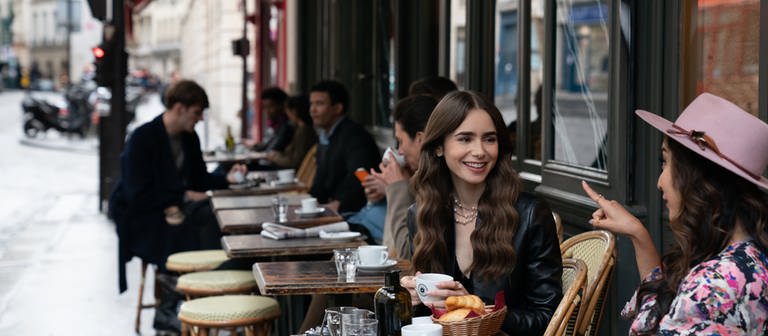 Emily (Lily Collins, M) sitzt mit einer Freundin im Café - eine Filmszene aus der ersten Staffel der Netflix-Serie «Emily in Paris» (undatierte Aufnahme). (Foto: dpa Bildfunk, picture alliance/dpa/Netflix © 2020 | Stephanie Branchu)