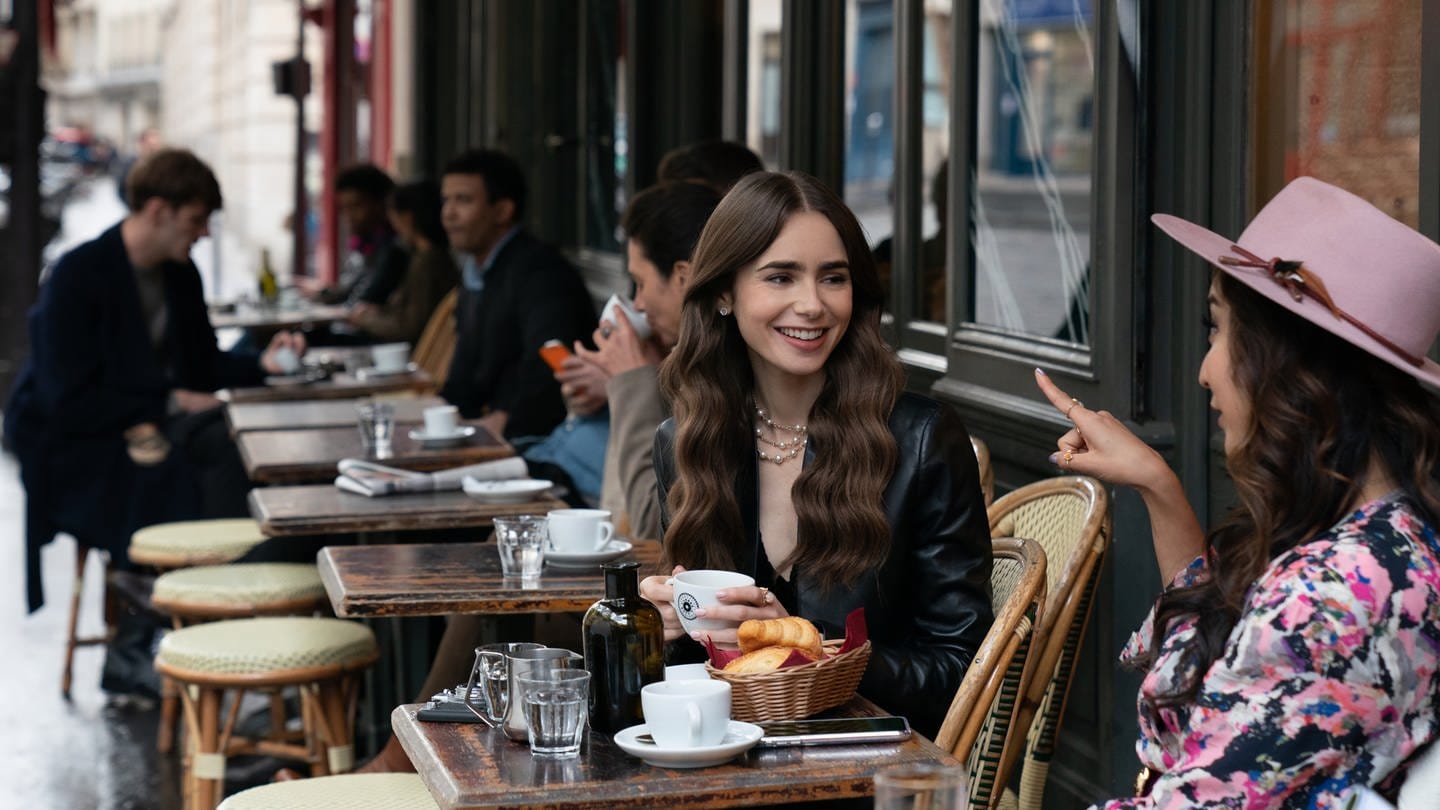 Emily (Lily Collins, M) sitzt mit einer Freundin im Café - eine Filmszene aus der ersten Staffel der Netflix-Serie «Emily in Paris» (undatierte Aufnahme). (Foto: dpa Bildfunk, picture alliance/dpa/Netflix © 2020 | Stephanie Branchu)