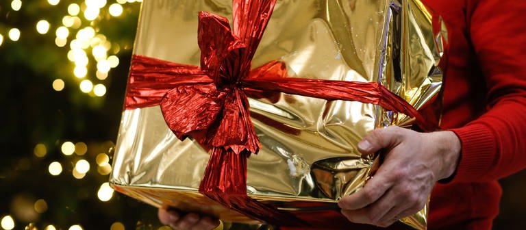 Ein Mann hält ein golden eingepacktes Weihnachtsgeschenk in den Händen (Foto: dpa Bildfunk, picture alliance/dpa | Gerald Matzka)