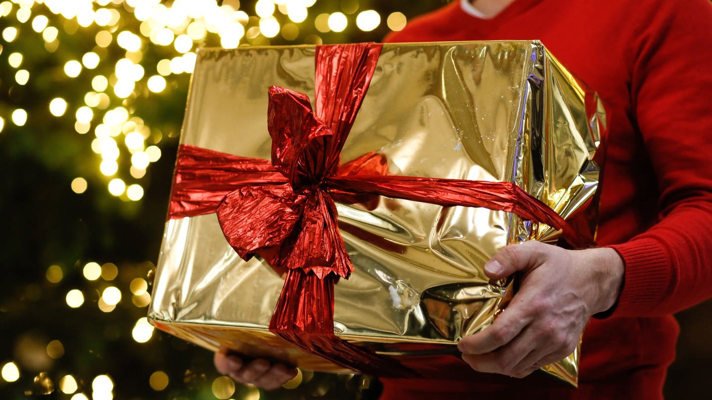 Ein Mann hält ein golden eingepacktes Weihnachtsgeschenk in den Händen