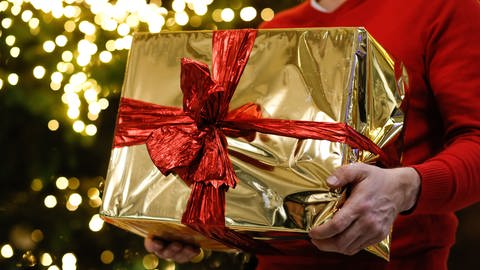 Ein Mann hält ein golden eingepacktes Weihnachtsgeschenk in den Händen (Foto: dpa Bildfunk, picture alliance/dpa | Gerald Matzka)