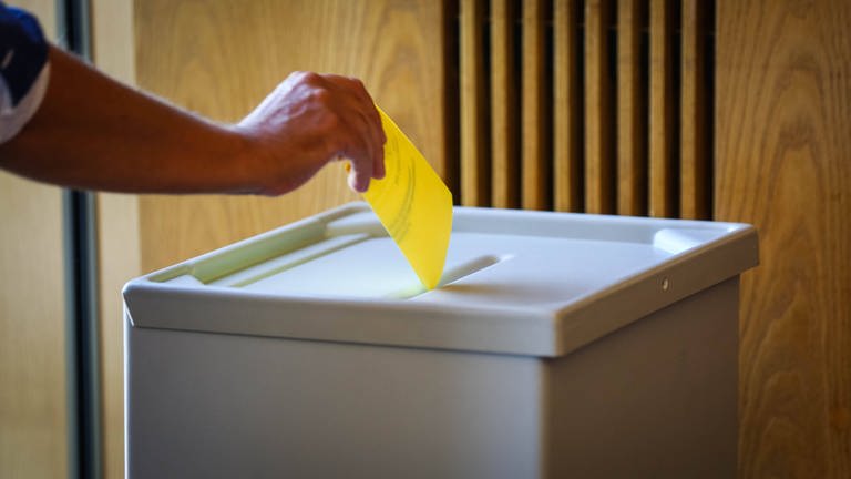 Symbolbild: Hand wirft Stimmzettel ein. (Foto: IMAGO, IMAGO / Sven Ellger)