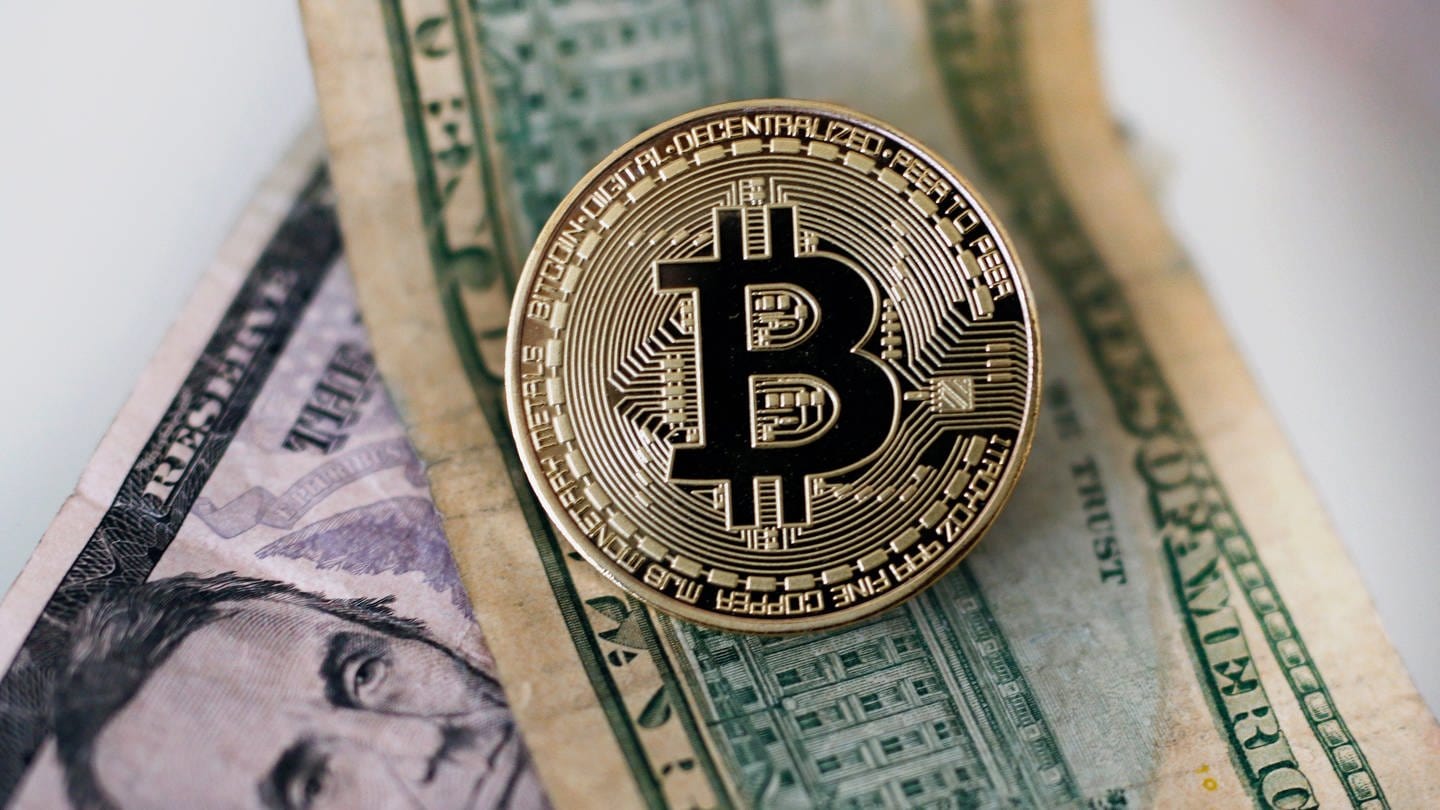 Eine Bitcoin Münze liegt auf Dollar Geldscheinen (gestellte Szene).