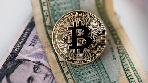 Eine Bitcoin Münze liegt auf Dollar Geldscheinen (gestellte Szene). (Foto: dpa Bildfunk, picture alliance/dpa | Ina Fassbender)