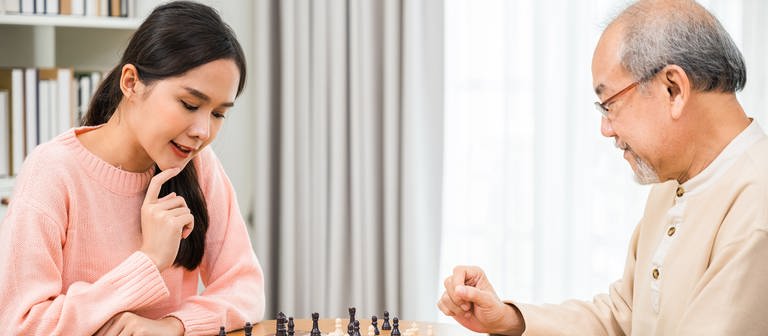 Young woman having fun sitting playing chess game with elderly senior at home. (Foto: IMAGO, IMAGO / Panthermedia)