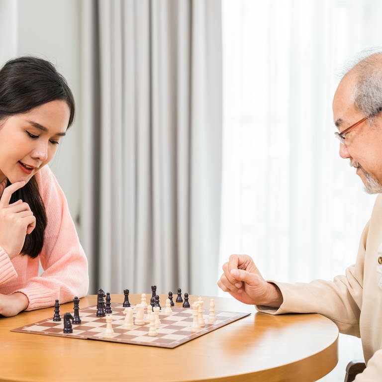 Young woman having fun sitting playing chess game with elderly senior at home. (Foto: IMAGO, IMAGO / Panthermedia)