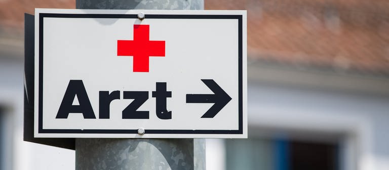 Ein Schild mit der Aufschrift «Arzt» hängt an einer Straßenlaterne. (Foto: dpa Bildfunk, picture alliance/dpa | Tom Weller)
