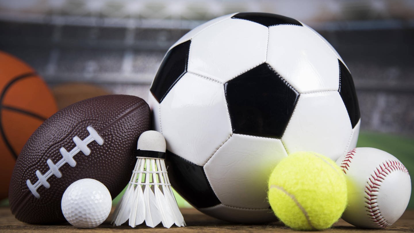 Verschiedene Sportbälle liegen nebeneinander - darunter ein Fußball, Basketball und ein Badmintonball.