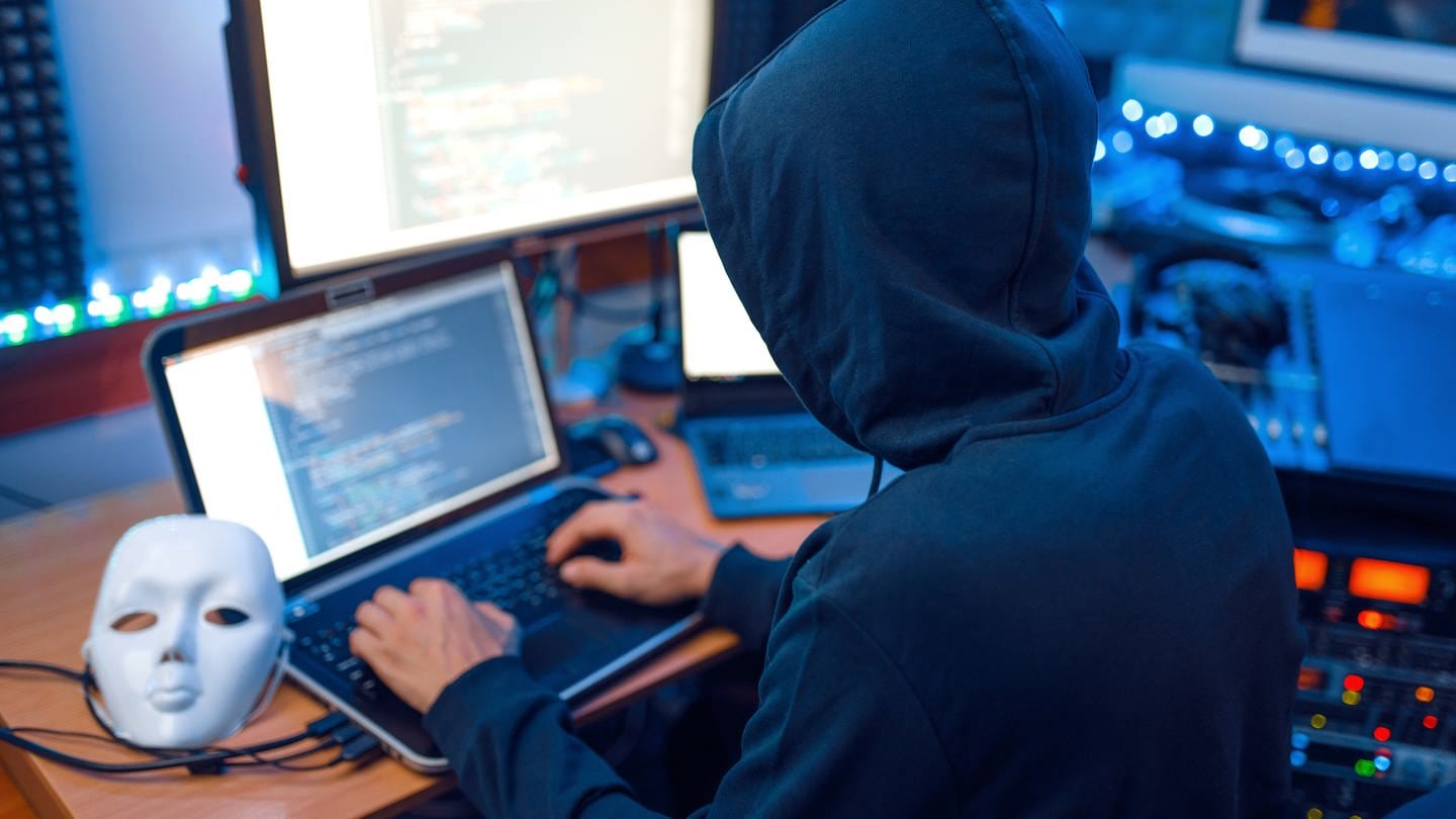 Hacker in mask and hood, account hacking, Hacker in mask and hood sitting at his workplace with laptop and PC, password or account hacking.