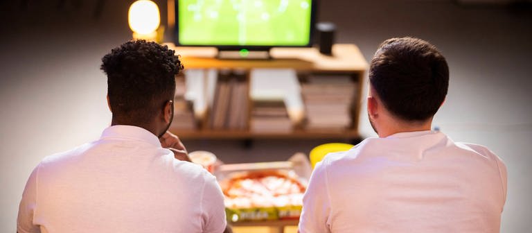 Young roommates watching football match together at home model released, Symbolfoto (Foto: IMAGO, IMAGO / Westend61)