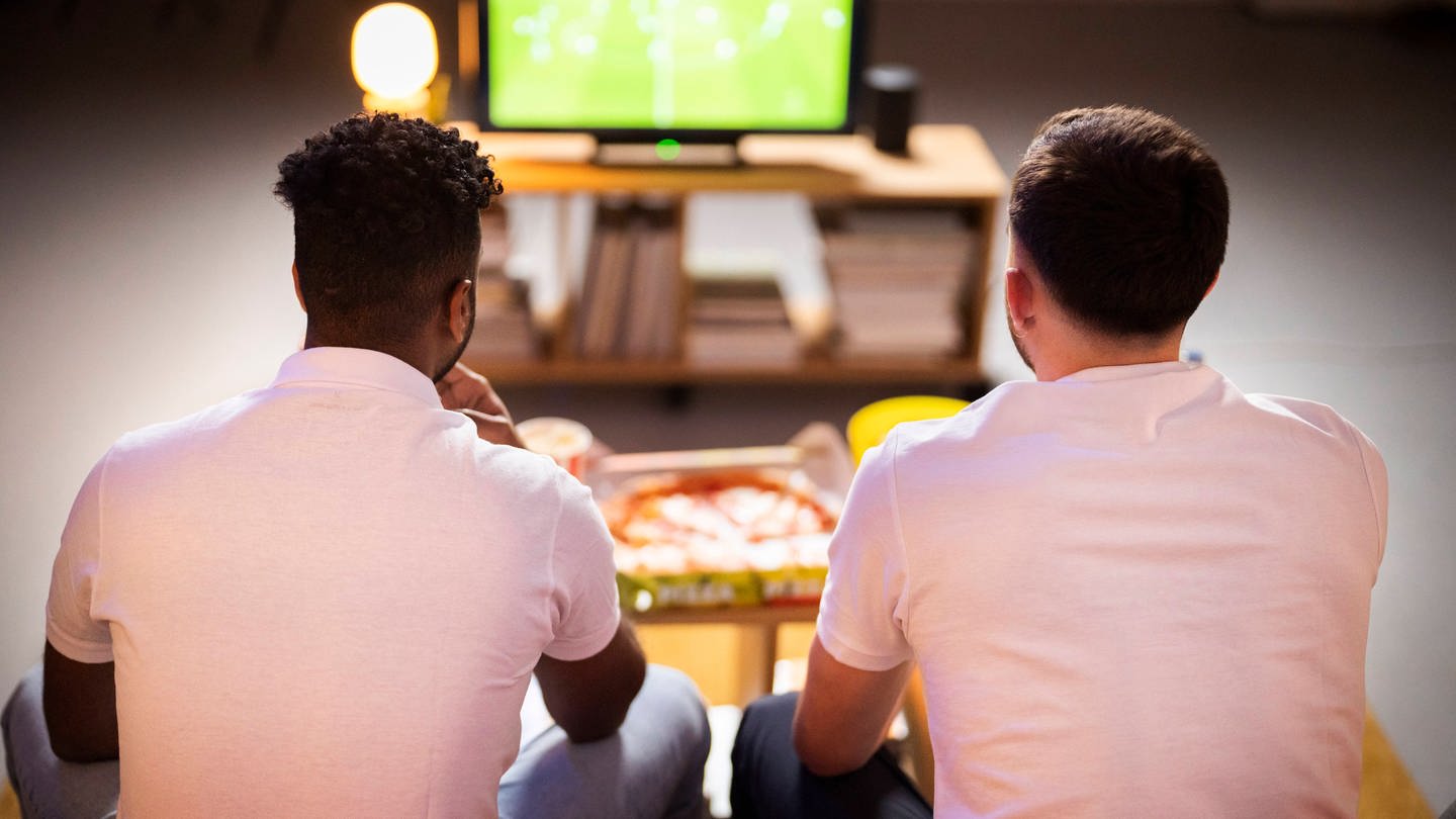 Young roommates watching football match together at home model released, Symbolfoto