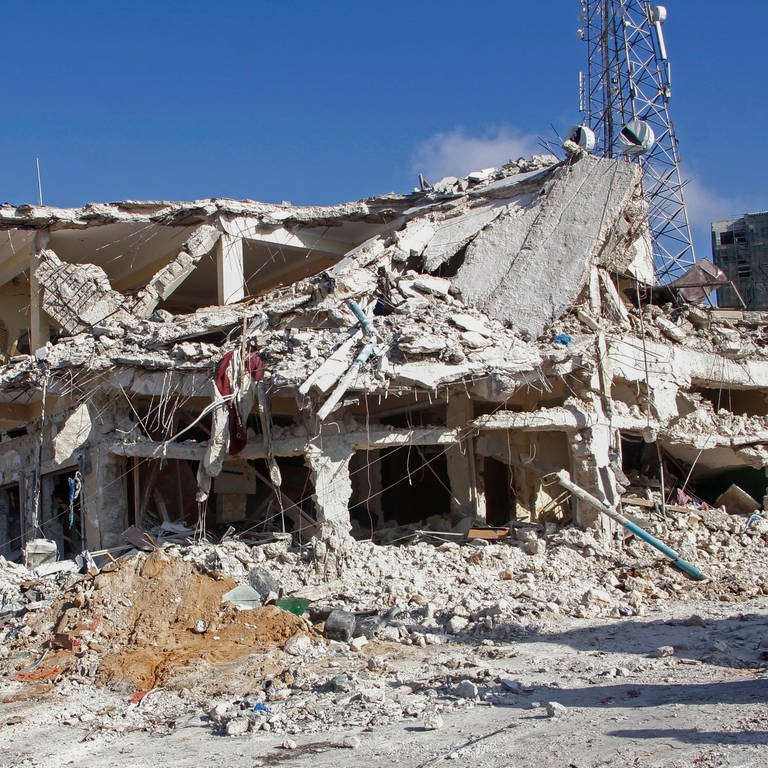 Menschen stehen vor einem zerstörten Gebäude an dem Ort, wo am Vortag zwei Autobombenanschläge an einer belebten Kreuzung in Mogadischu in Somalia stattgefunden haben. Bei den zwei Selbstmordanschlägen sind nach Angaben des Präsidenten mindestens 100 Menschen getötet und 300 verletzt worden. (Foto: dpa Bildfunk, picture alliance/dpa/AP | Farah Abdi Warsameh)