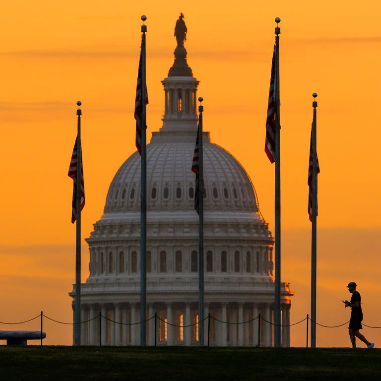 Ein Fußgänger geht während des Sonnenaufgangs an den US-Flaggen auf der National Mall und am US-Kapitolgebäude vorbei. (Foto: dpa Bildfunk, picture alliance/dpa/AP | J. David Ake)