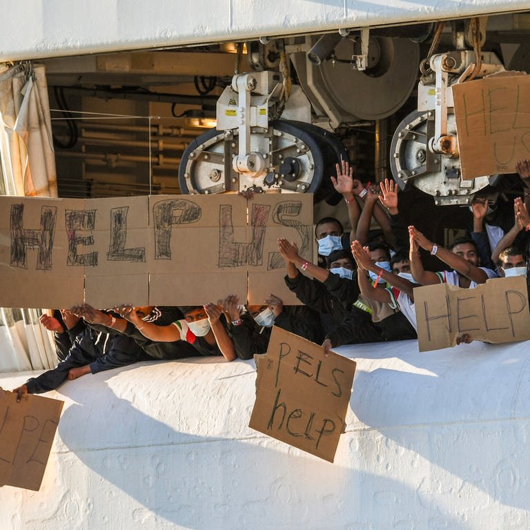 Migranten halten Transparente mit der Bitte um Hilfe an Deck des unter norwegischer Flagge fahrenden Schiffes «Geo Barents», das von «Ärzte ohne Grenzen» betrieben wird, im Hafen von Catania (Foto: dpa Bildfunk, picture alliance/dpa/AP | Salvatore Cavalli)